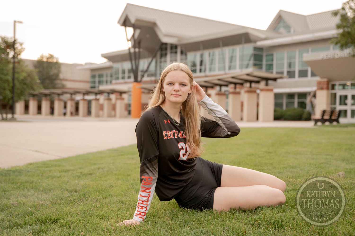 Student in black Central College athletic wear poses on green lawn in front of modern campus building.