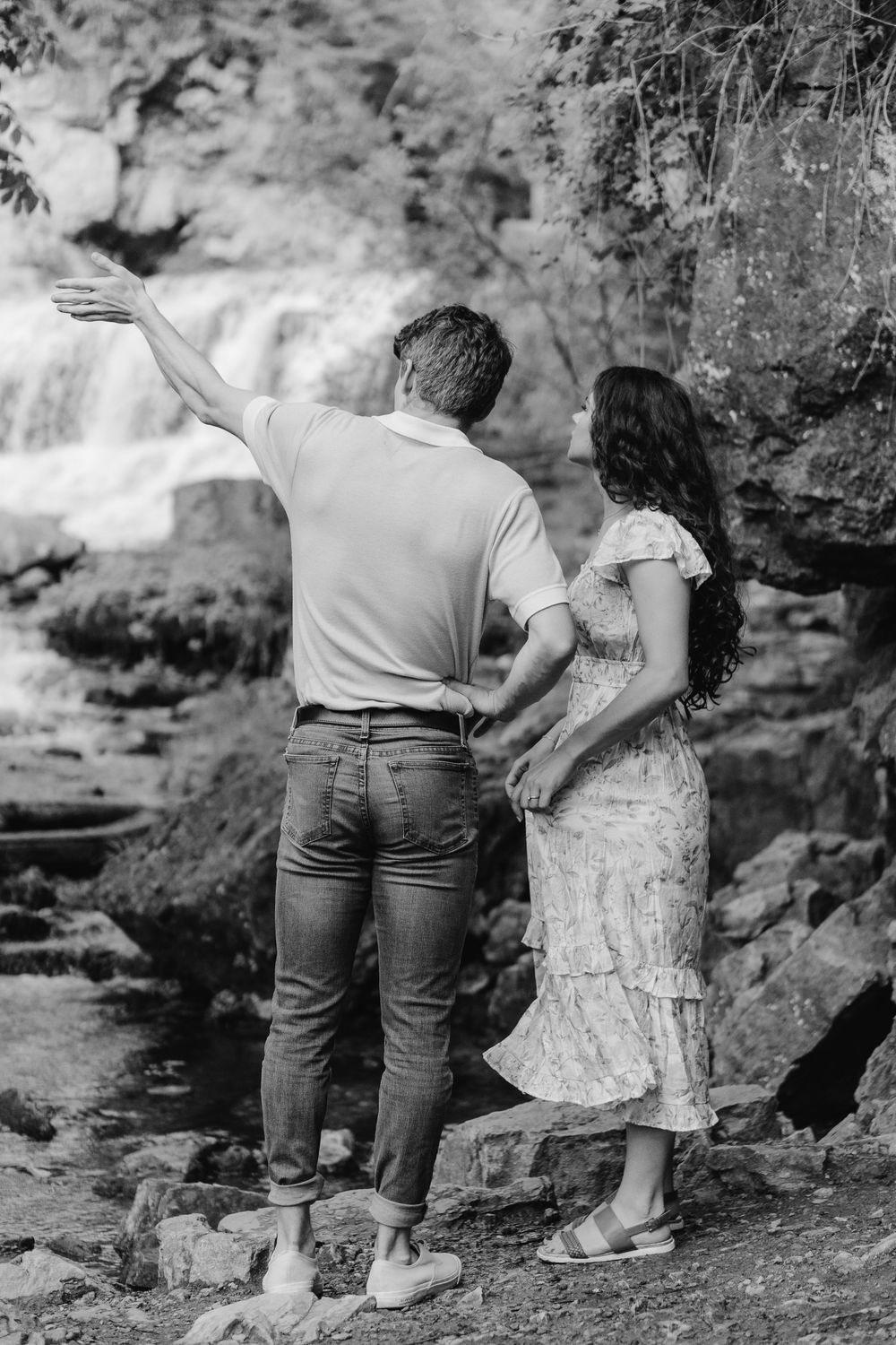 Bride-to-be pointing into the distance as they explore together during their forest engagement shoot