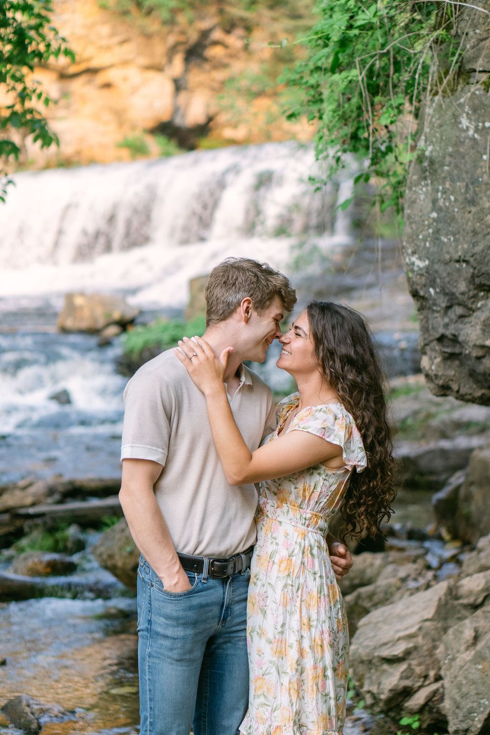 Bride-to-be in a flowy dress gazing at her fiancé during a golden hour engagement session at Willow River State Park and gentle embrace