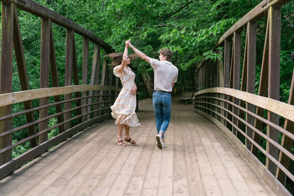 Couple dancing and twirling on a wooden bridge with lush green trees behind them at Willow River State Park