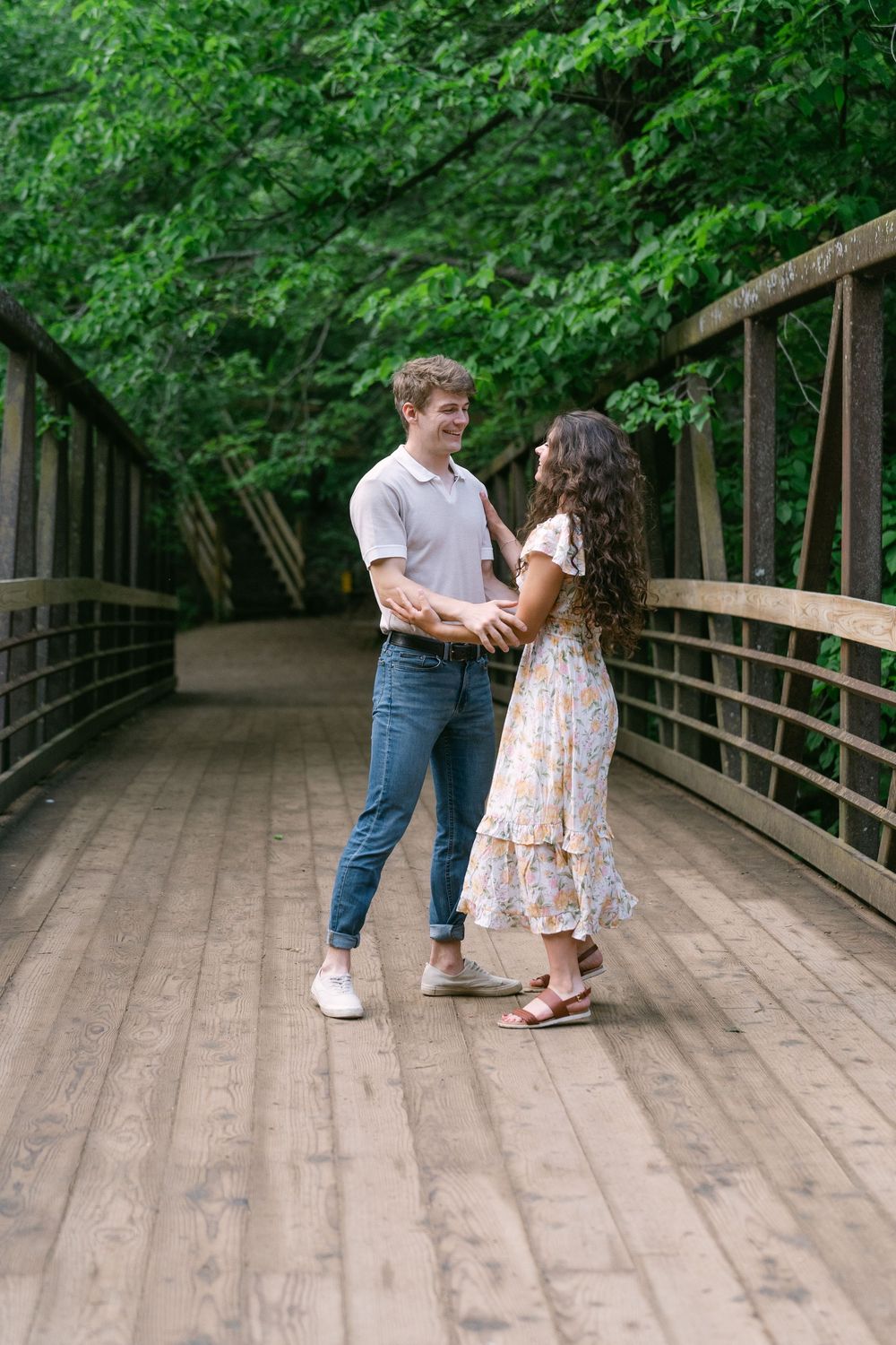 couple laughing and dancing on a wooden bridge with lush green trees behind them at Willow River State Park