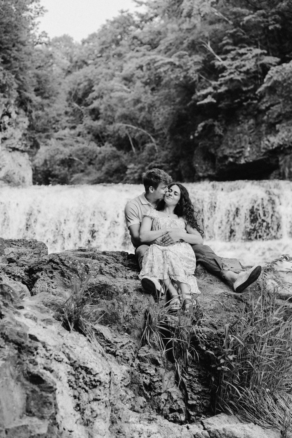 Romantic kiss on a rocky overlook framed by waterfalls and bright forest at Willow River in Hudson, Wisconsin