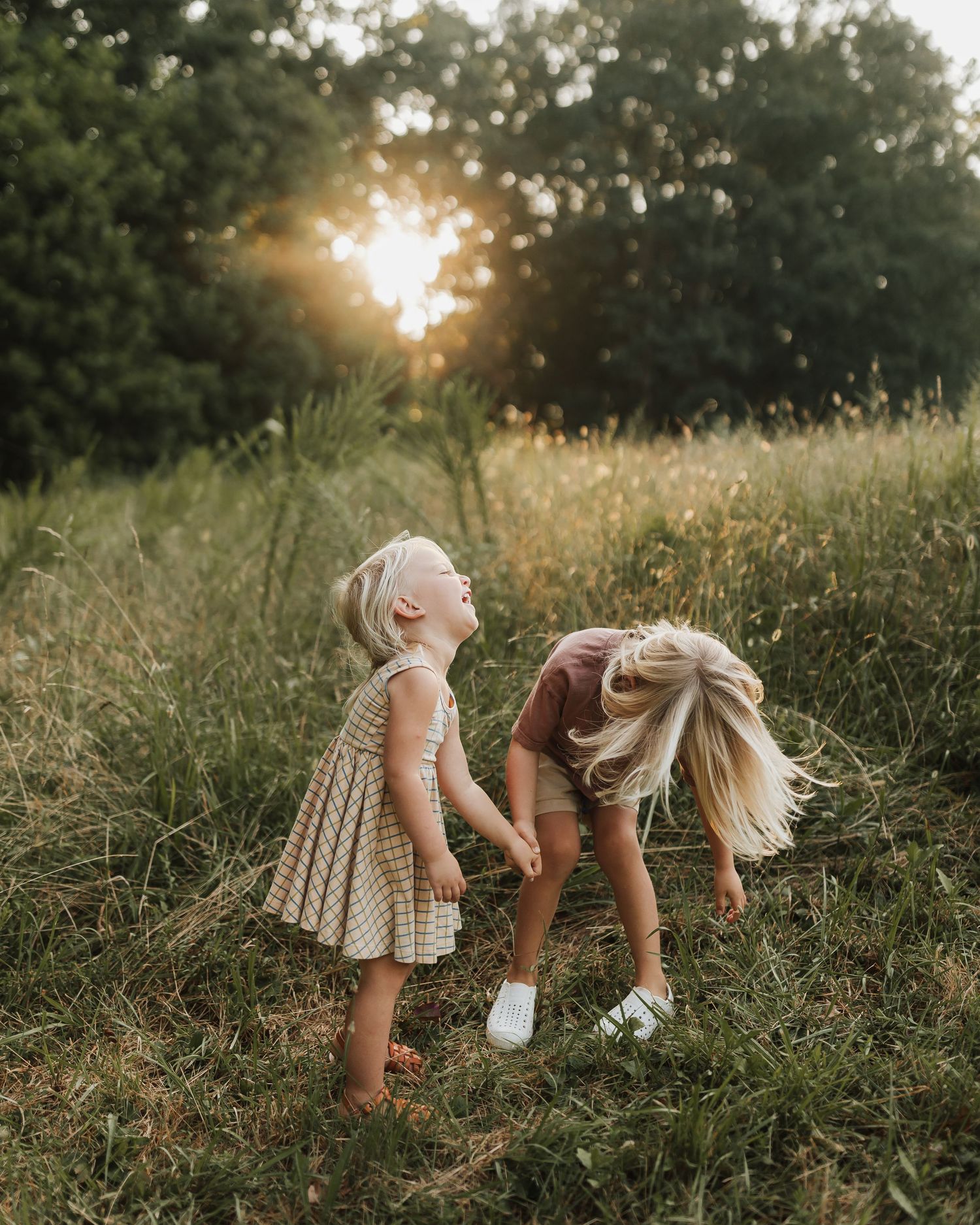 A dreamy sunset scene in a meadow with two figures in light dresses exploring the tall grass on a warm evening.