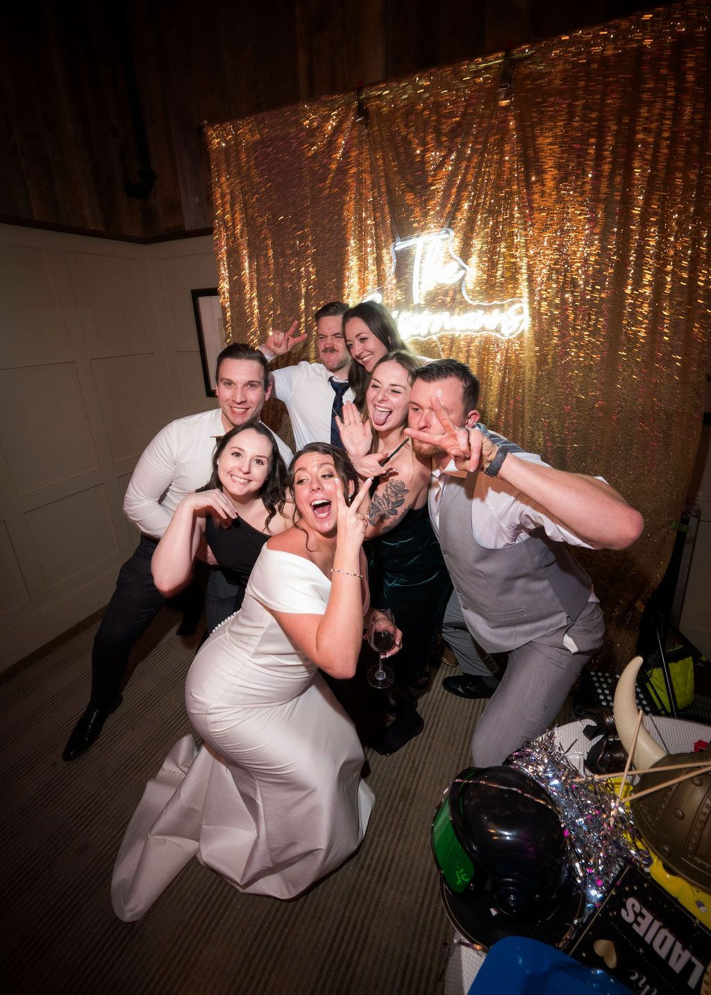 Wedding party poses playfully against a gold sequin backdrop at a reception venue.