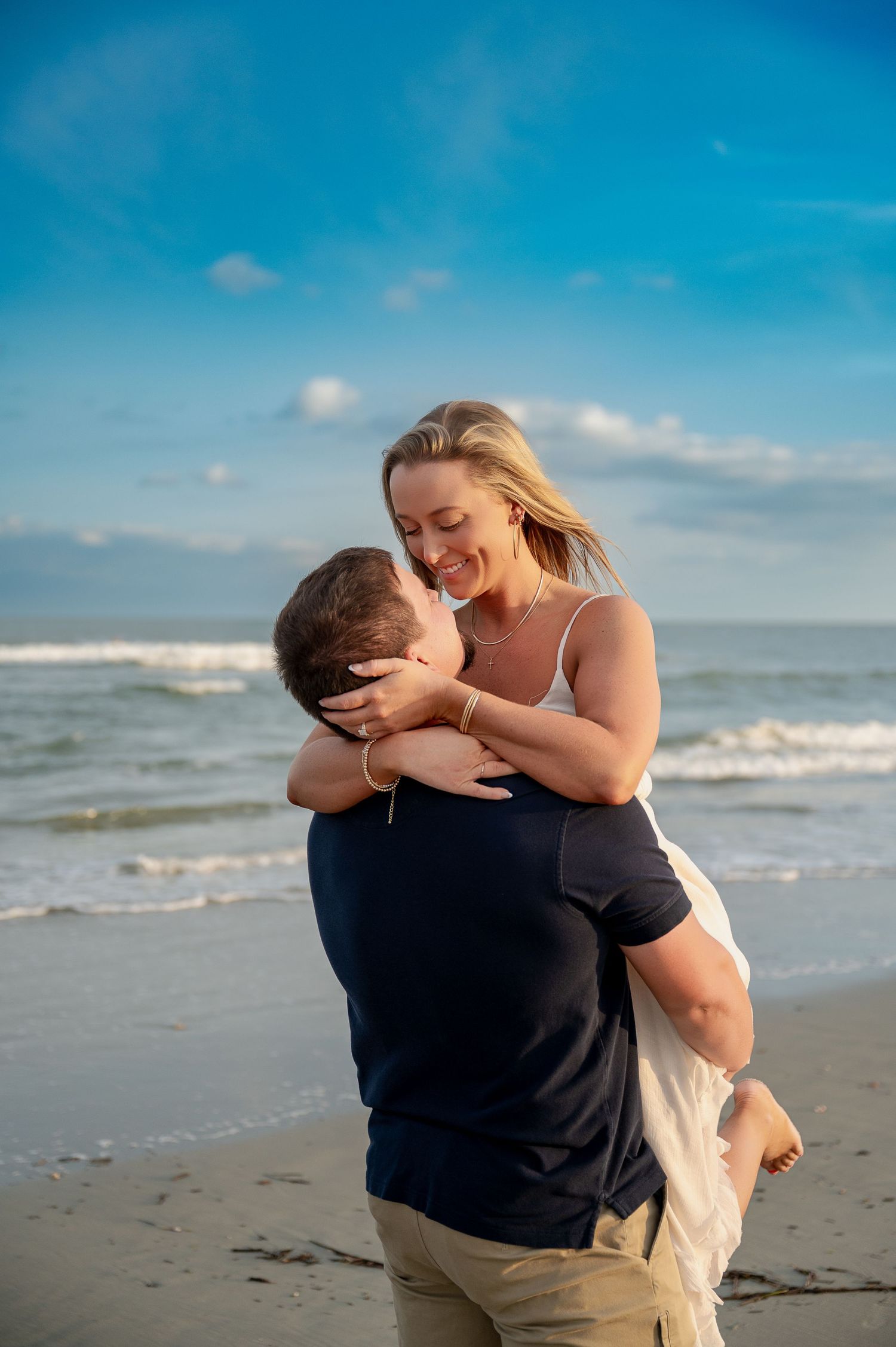 Joyful couple embracing on sunny beach with ocean waves in background.