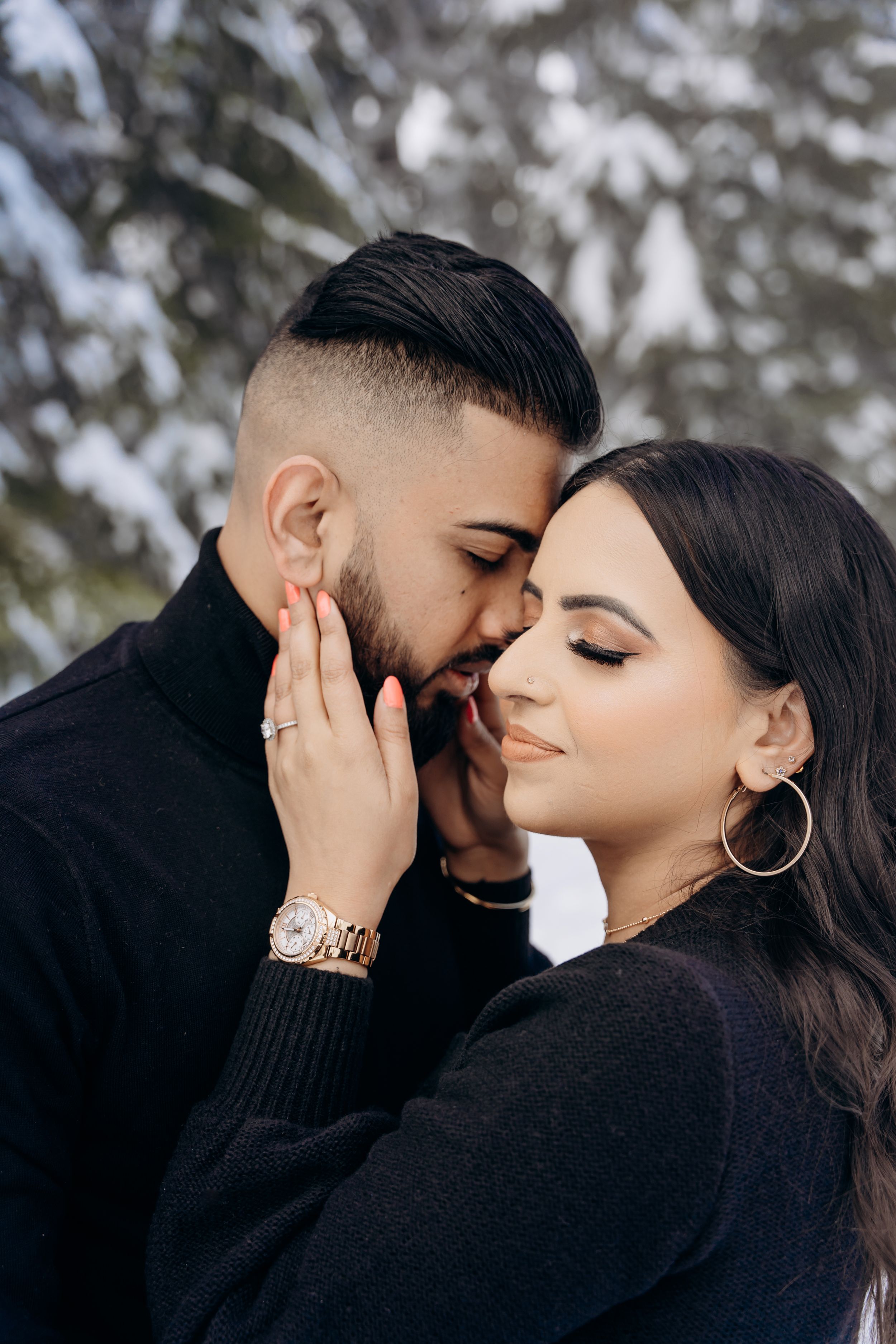 A romantic couple shares an intimate moment in matching black outfits against a blurred winter background.