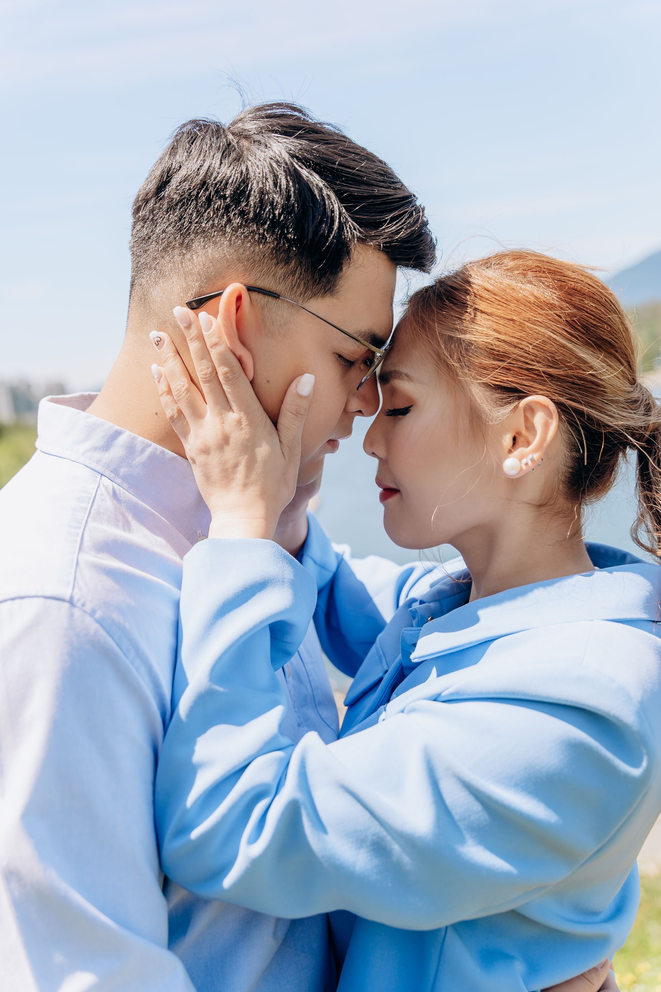 A romantic couple in matching light blue outfits share an intimate kiss against a scenic outdoor backdrop.