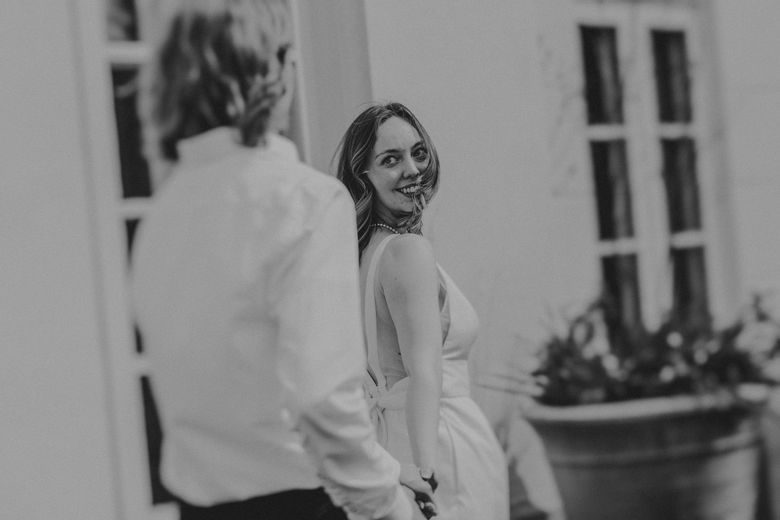 Black and white photo of a person looking back over their shoulder with a joyful expression outside a building.