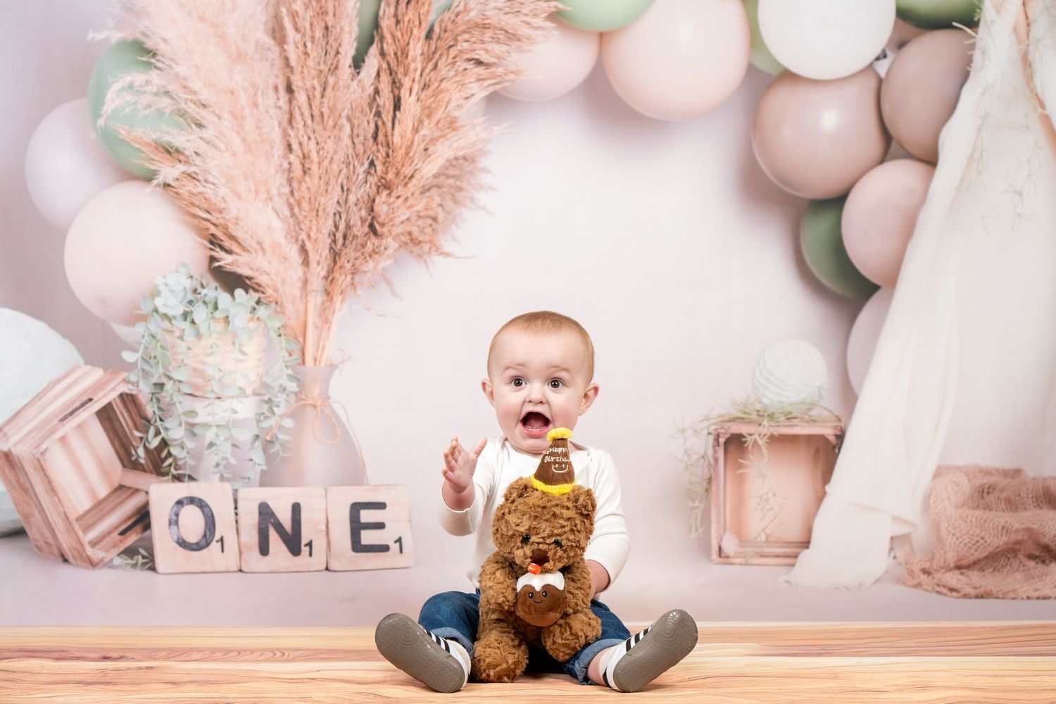 A first birthday cake smash photo session setup with pink pampas grass, balloons, and teddy bear decorations.