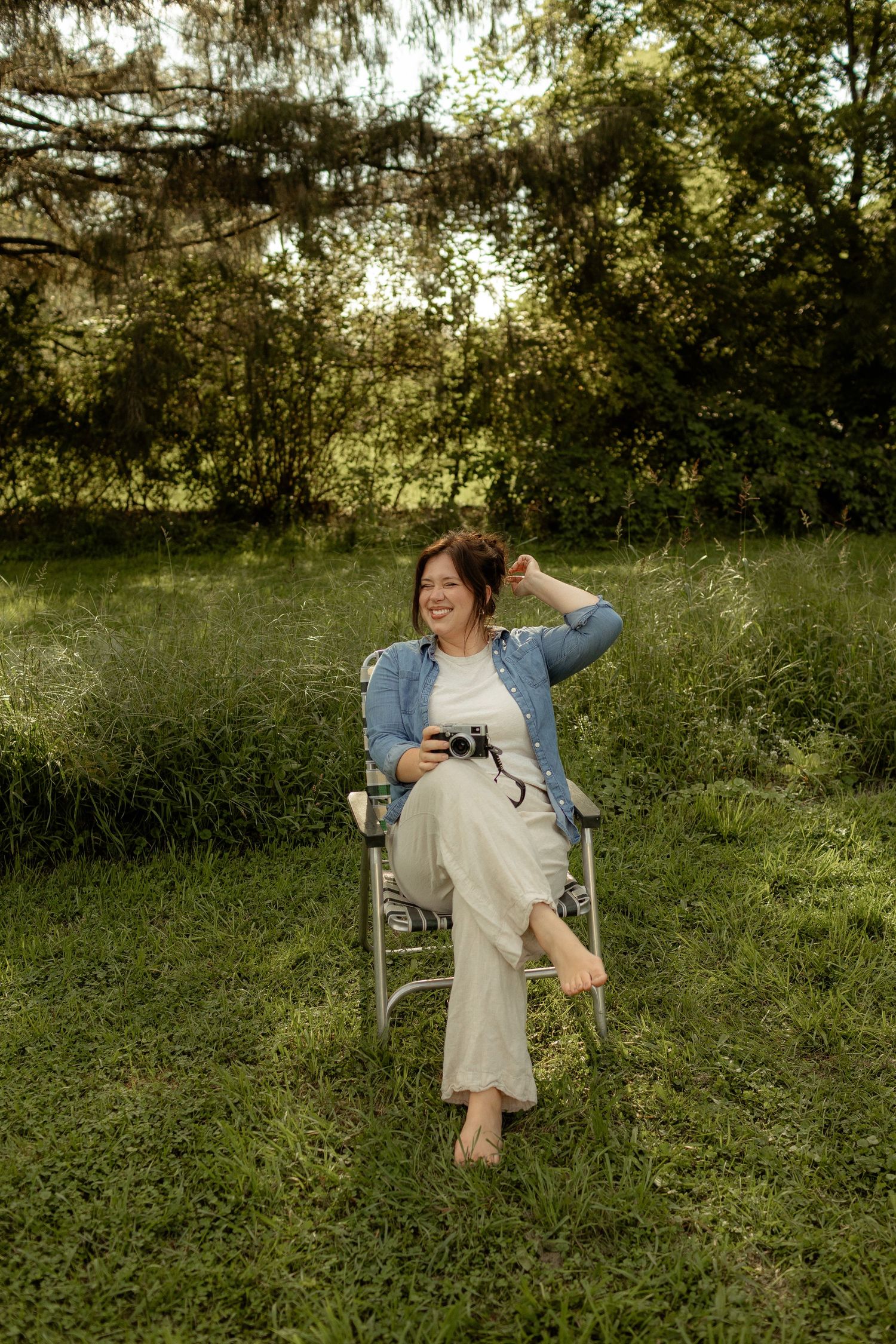 Joyful photographer poses with vintage Polaroid camera while sitting on wooden chair.