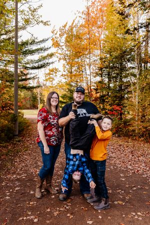 Family of three posing playfully on a leaf-covered path surrounded by colorful autumn trees.