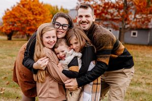 Happy family of five sharing a group hug outdoors surrounded by colorful autumn trees.