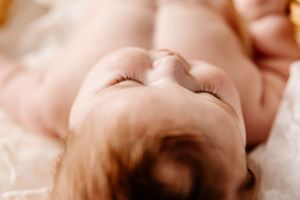 Close-up portrait of a sleeping newborn baby with soft skin and delicate features resting peacefully on a white blanket.