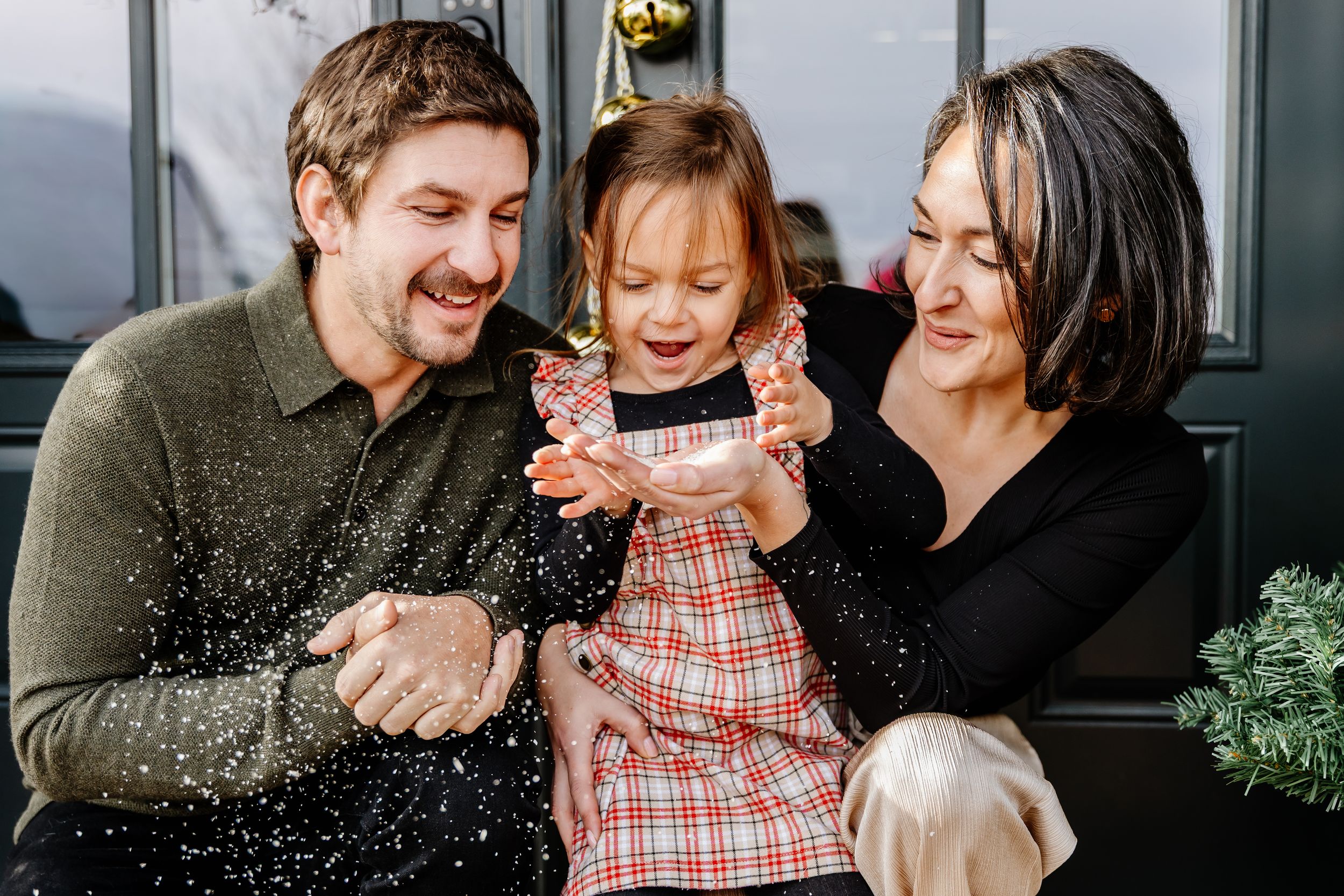 Happy family with young daughter celebrating outdoors with glitter confetti.