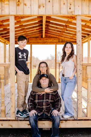 Family of four posing inside a wooden gazebo structure, with two teens standing and parents seated together.