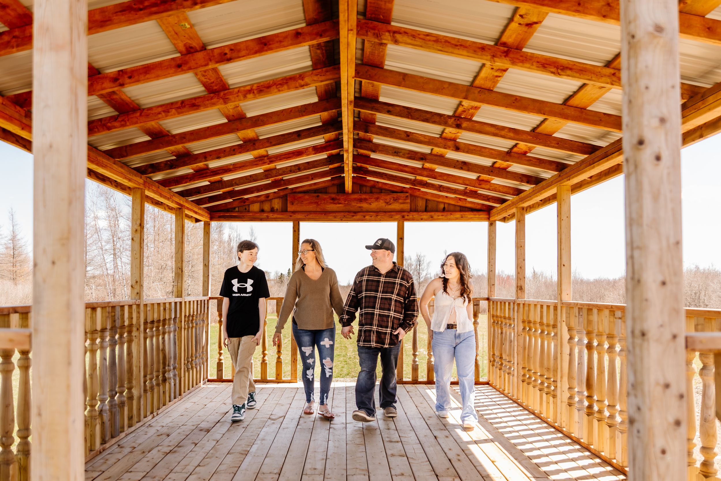 Family of four walking together under a rustic wooden covered bridge on a sunny day.