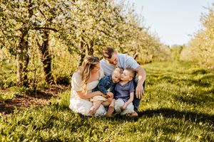 Family of four sharing a joyful moment together in a blooming apple orchard on a sunny spring day.