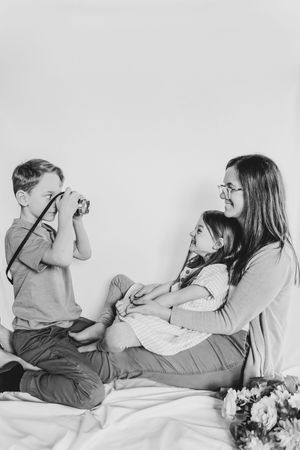 Black and white photo of a mother with two children as boy photographs them with a camera.