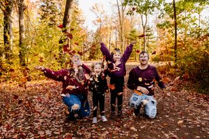 Family of five tossing autumn leaves in the air on a colorful fall forest path.
