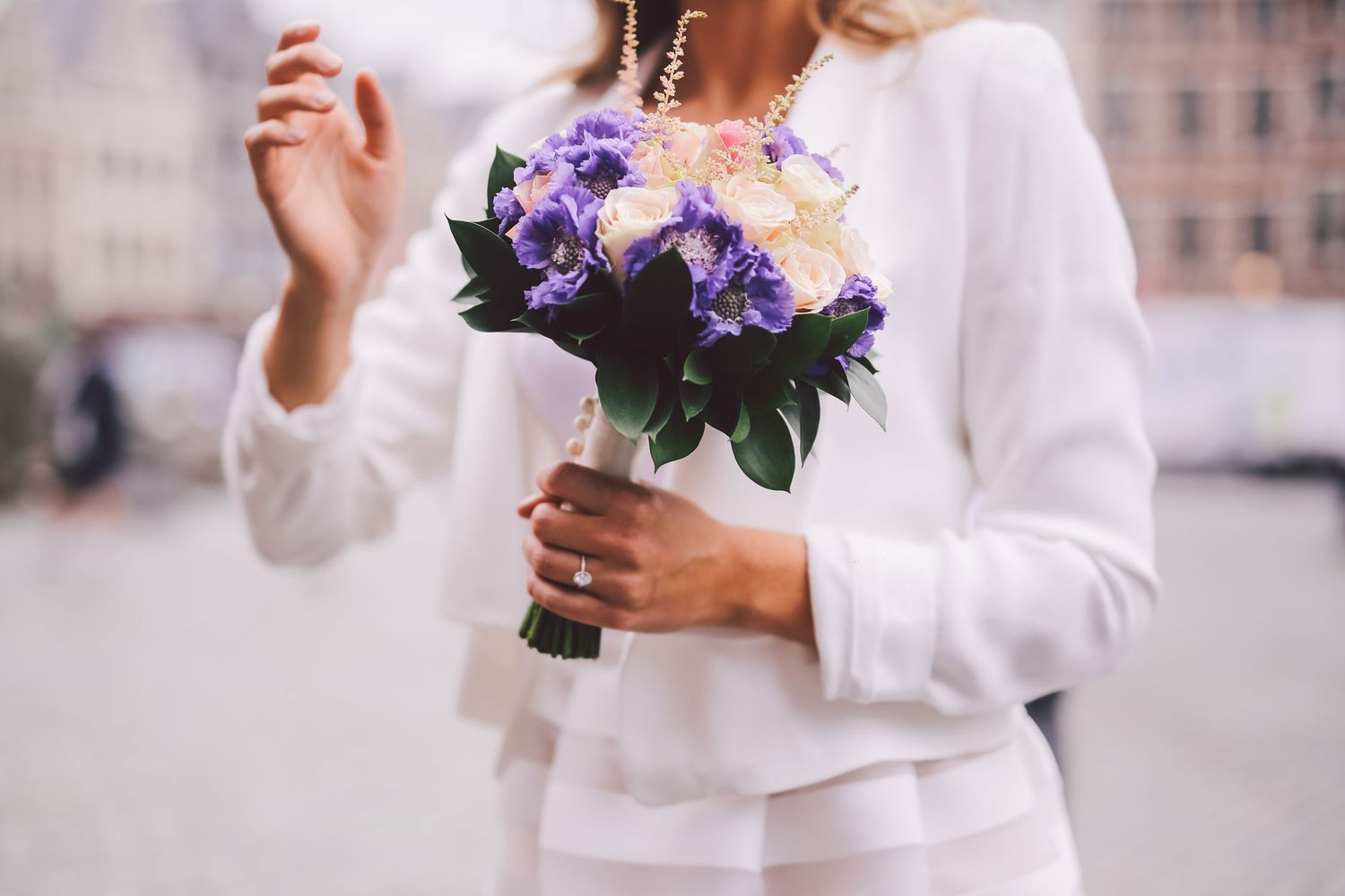 Person wearing a white wedding dress holds their hands together while showing a peace sign gesture in a natural pose.