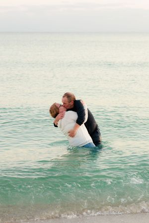 A romantic couple shares a passionate kiss while dipping in turquoise ocean waters at the beach.