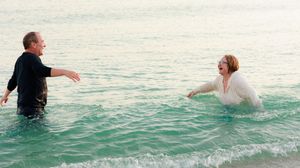 A couple playing and splashing in the shallow turquoise ocean water near the beach.
