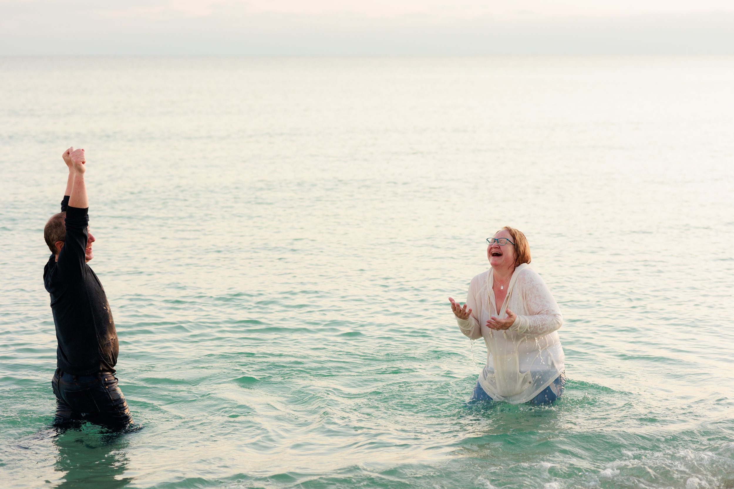 A couple sits in shallow ocean water creating a serene and romantic scene at dusk.