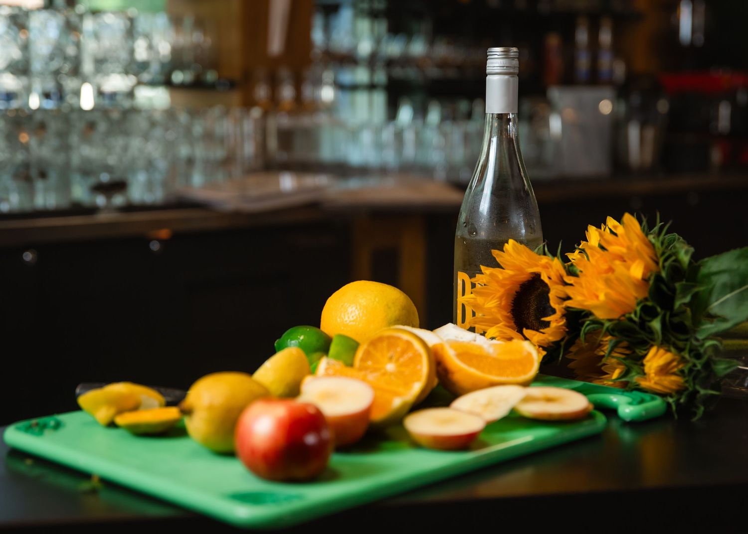 Citrus fruits and sunflowers arranged on a dark wooden surface with a green cutting board in moody lighting.