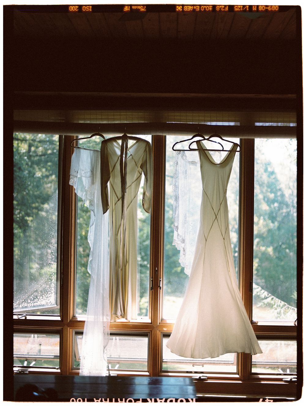 White wedding dresses hang elegantly against sunlit windows in a rustic room.
