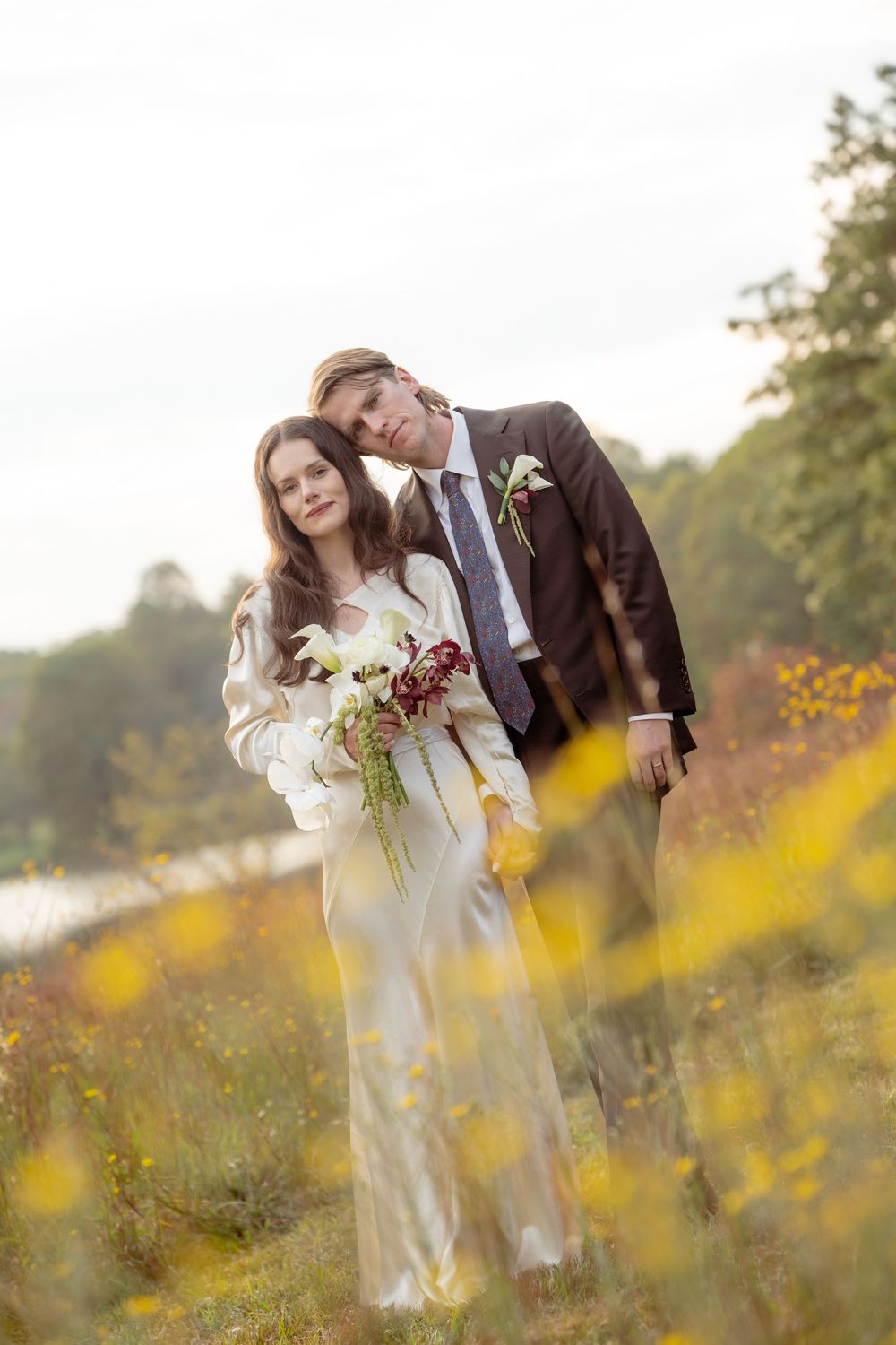 A romantic couple embraces in a sunlit meadow of yellow wildflowers during a golden hour photoshoot.