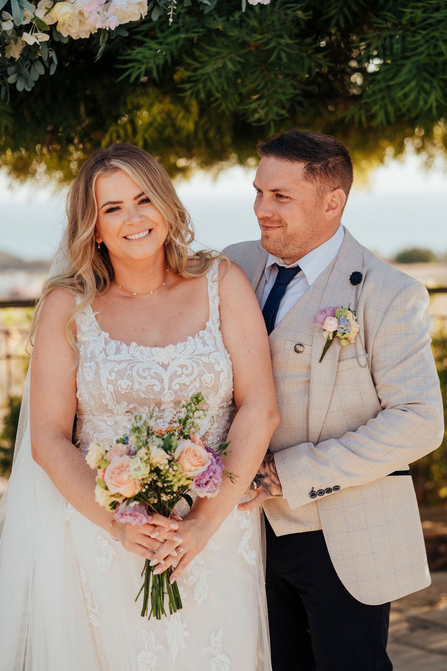 A romantic wedding moment captured among lush greenery with two people embracing in formal attire.
