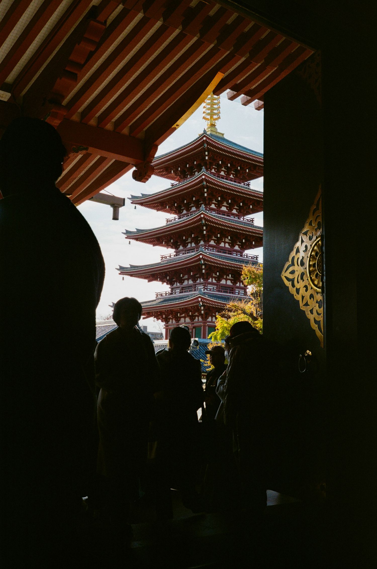 View of a traditional five-story Japanese pagoda through a temple gateway with silhouetted visitors in the foreground.