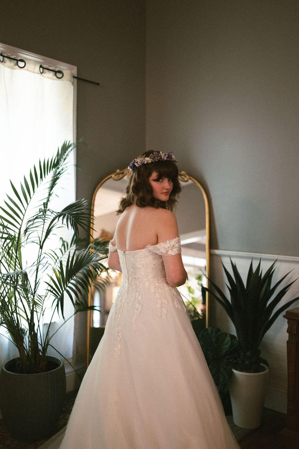 a bride stands in front of a mirror and poses looking at the camera