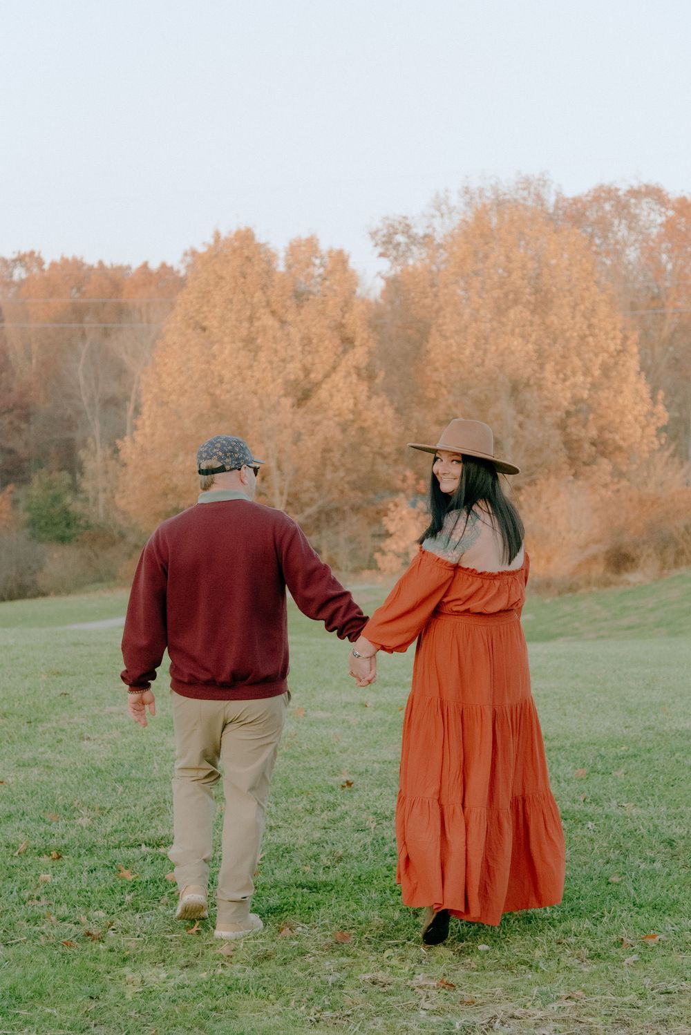 Couple walking hand in hand through a green field on an autumn afternoon.