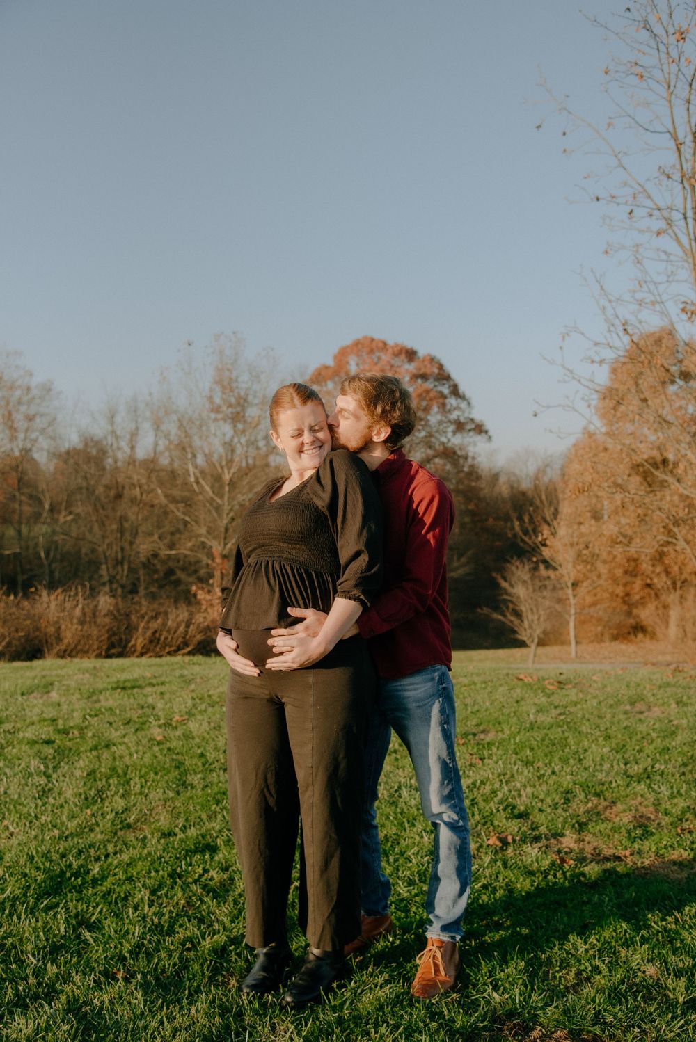 Intimate family moment captured in golden afternoon light with autumn trees in background.