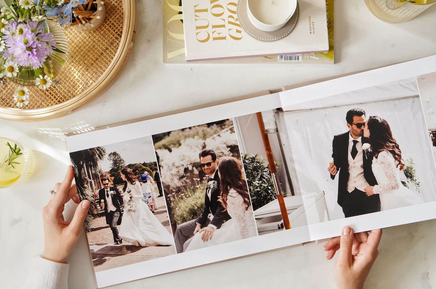 Hands holding open a wedding photo album with printed photographs showing romantic moments from a celebration.