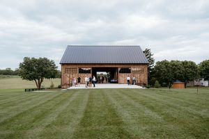 Modern rustic barn venue with brick exterior and metal roof sits on a manicured green lawn under cloudy skies.