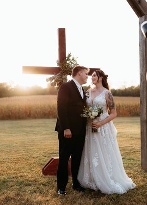 A couple in wedding attire shares an intimate sunset moment in a golden field at dusk.