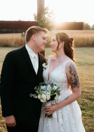 Newlyweds share an intimate moment in golden sunlight while holding white floral bouquets.
