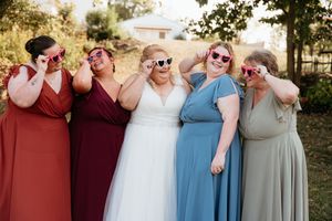 A group of people in coordinated wedding attire stand together making heart shapes with their hands in an outdoor setting.