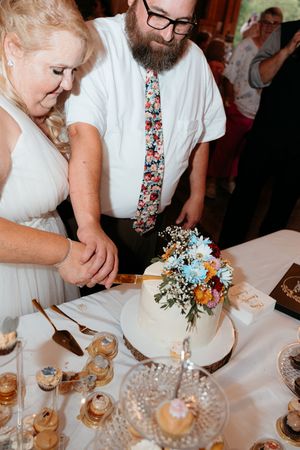 Couple enjoying desserts and drinks at an elegant wedding reception with floral centerpieces and white tablecloths.