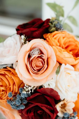 Close-up macro photo of pink, burgundy, and orange roses with delicate white baby's breath flowers in a wedding bouquet.