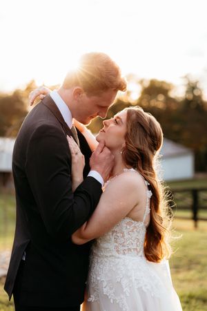 Bride and groom share a romantic golden hour moment outdoors, with the groom gently holding the bride's face as they lean in close.