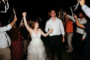 Bride and groom hold hands walking through sparkler exit at outdoor wedding reception at night.