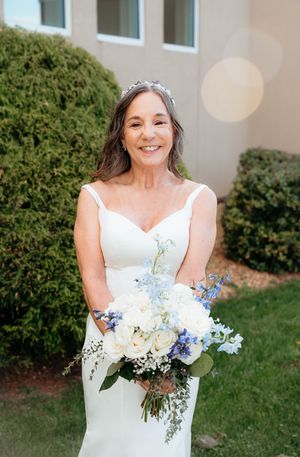 A bride in a white wedding dress holds a beautiful bouquet of white and blue flowers against a garden backdrop.