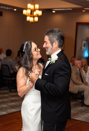 A couple dances together at a wedding reception under warm lighting in a ballroom.