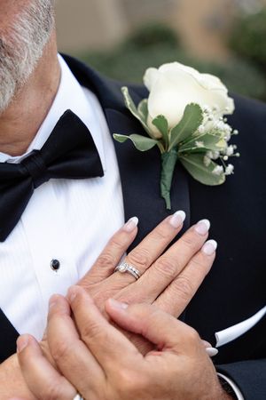 Close-up of white rose boutonniere pinned to black tuxedo lapel with hands adjusting the flower.