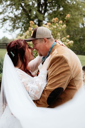 Bride and groom share a romantic moment outdoors, with her white veil flowing as they lean in for a kiss.