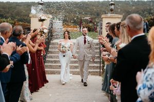 Wedding guests celebrate with sparklers as newlyweds walk through tunnel of light at outdoor evening reception.