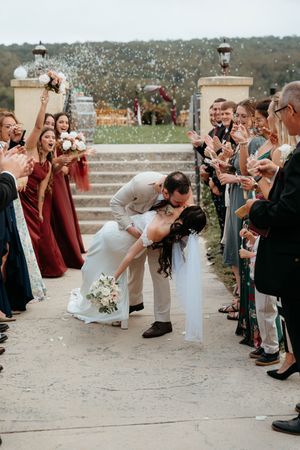 Wedding party guests line up outdoors for a celebratory moment as newlyweds share a romantic dip kiss.